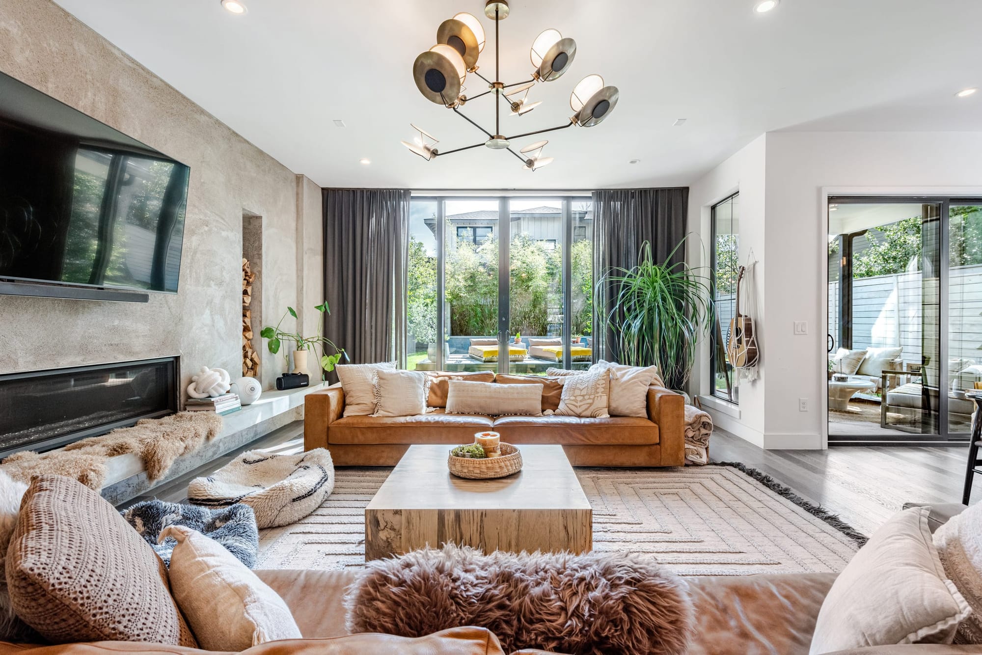 The living room at The Hether Haus — camel leather sofas with sheepskin throws, a chunky wood coffee table, and a plaster fireplace wall beside glass doors to the backyard