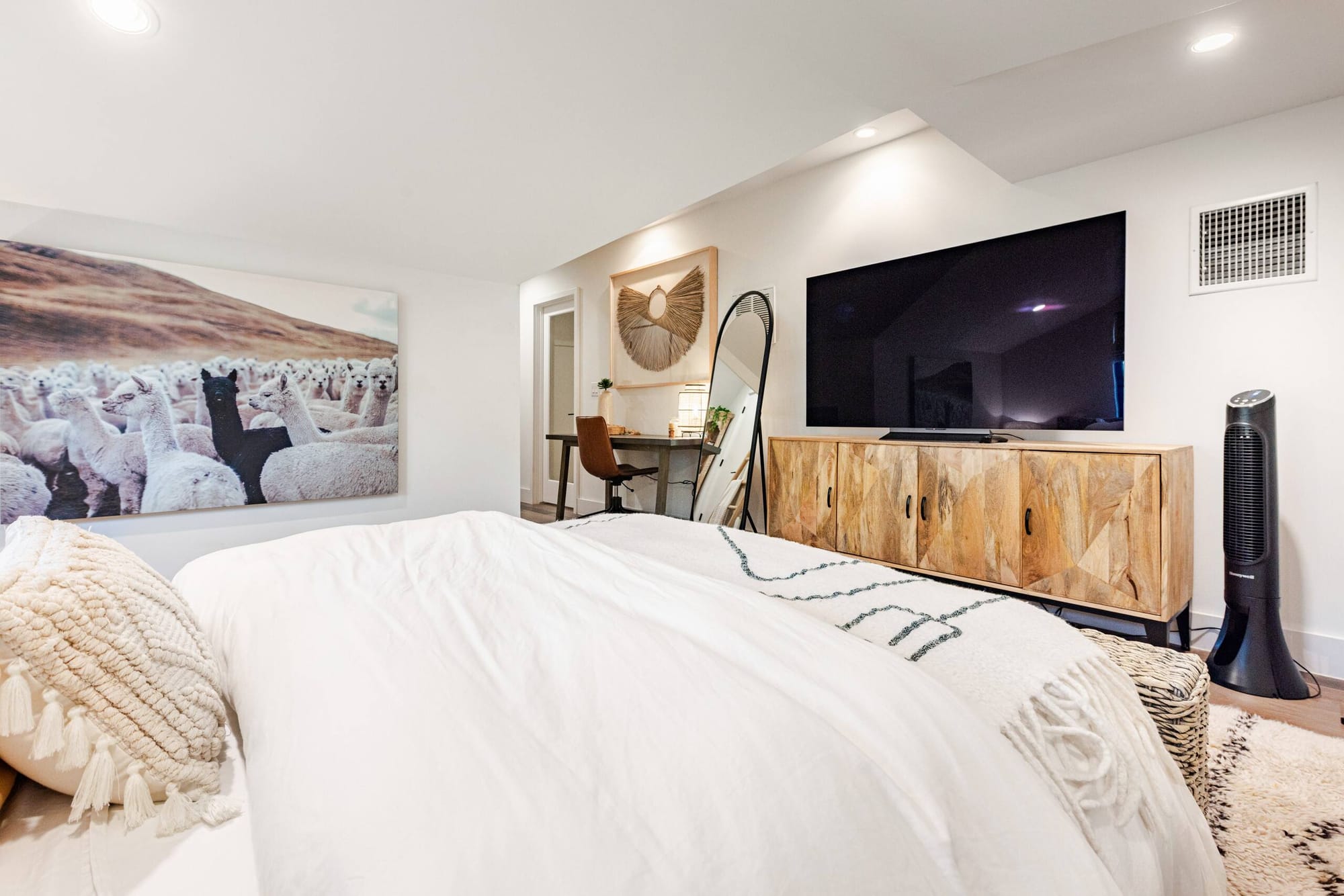 A guest bedroom — an alpaca art print above a rustic wood media console, with an arched mirror in the corner