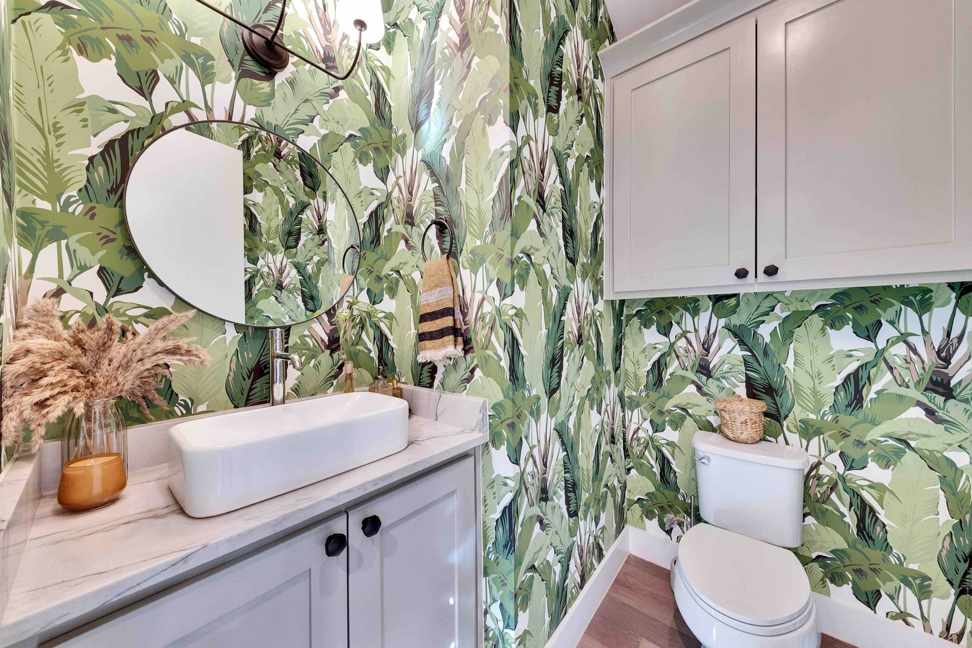 The powder room wrapped in banana-leaf botanical wallpaper, with a vessel sink and round mirror