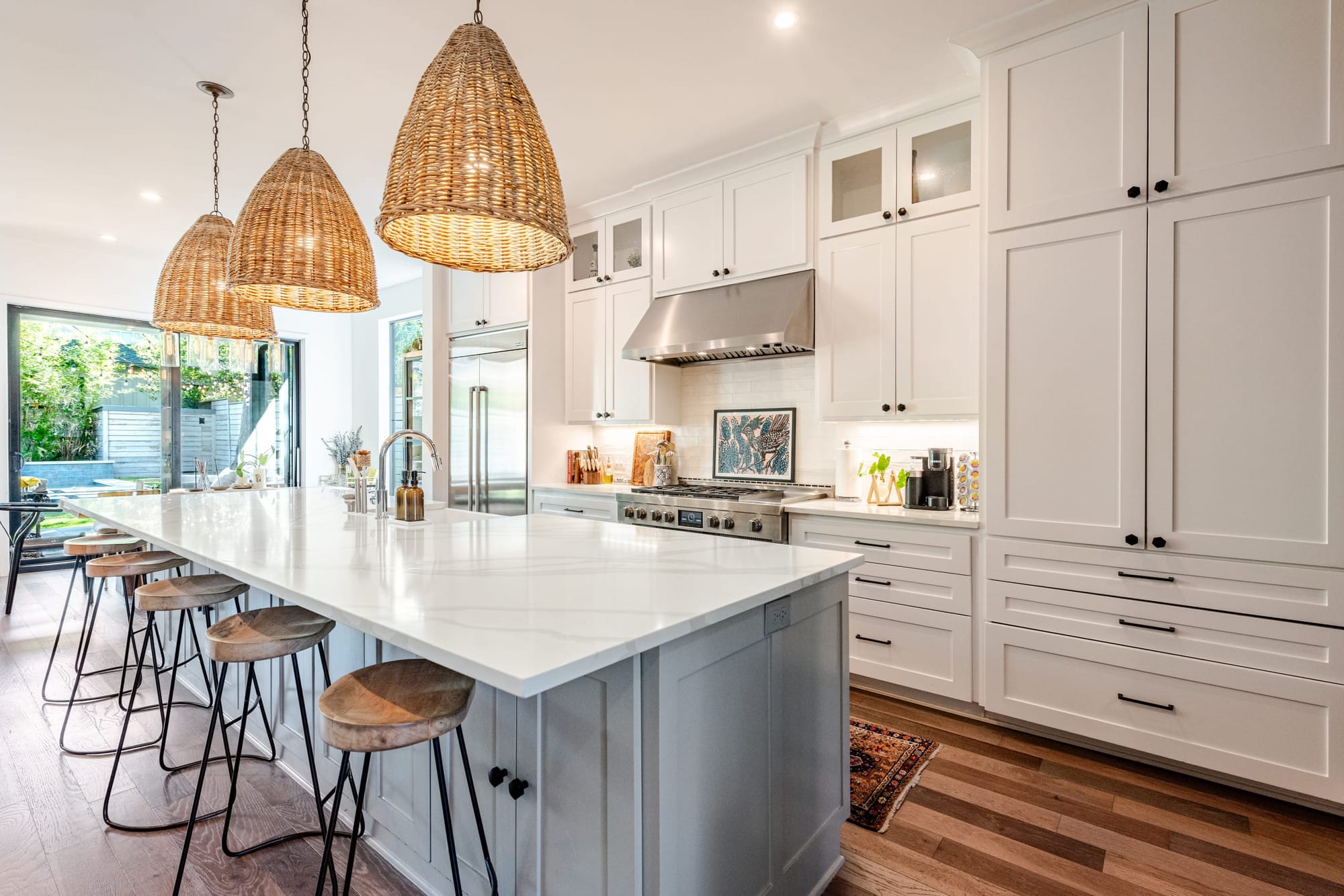 The kitchen — a marble island under rattan basket pendants, white shaker cabinetry, and a stainless range